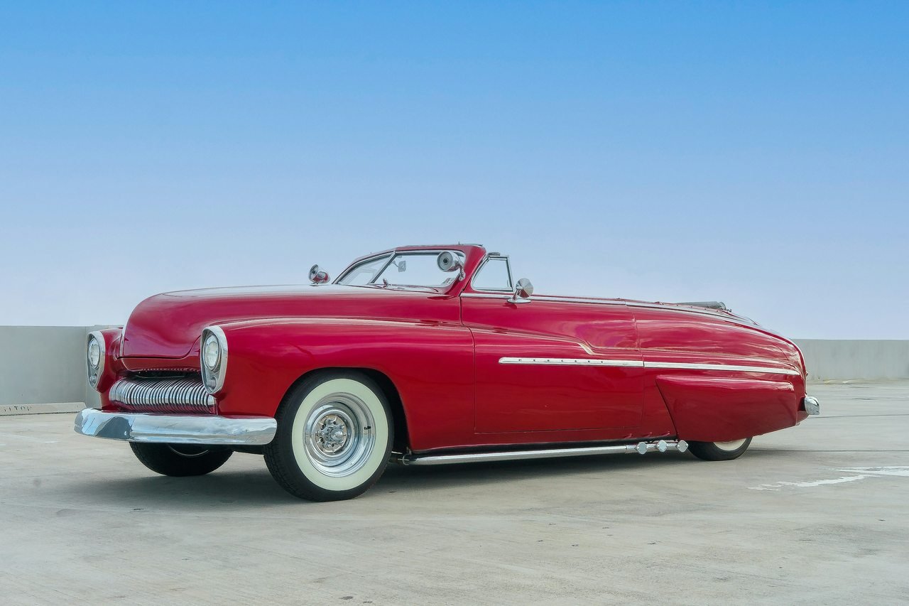Low red custom convertible with whitewall tires parked in an open lot.